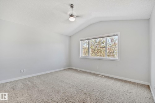Spacious room featuring vaulted ceilings, a contemporary ceiling fan with integrated lighting, expansive window, light-colored carpeting, and neutral wall paint - 614 Mcdonough Link, Edmonton, AB 