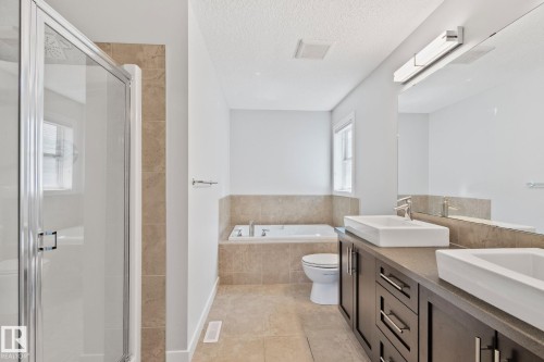 Bathroom featuring a dual vanity with vessel sinks, a walk-in shower with clear glass enclosure, a built-in soaking tub, and tile flooring - 614 Mcdonough Link, Edmonton, AB 