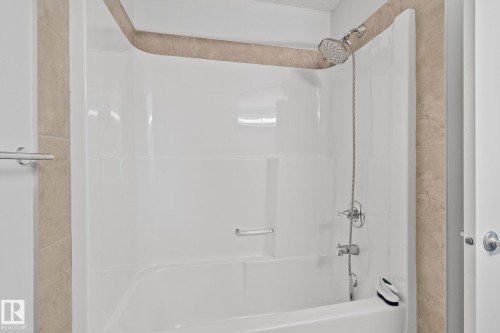 White acrylic tub and shower combination with a handheld shower head, complemented by beige-toned tile surround - 614 Mcdonough Link, Edmonton, AB 