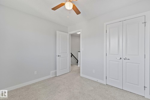 Carpeted room with a ceiling fan light fixture, light gray wall paint, white baseboards, and white paneled doors - 614 Mcdonough Link, Edmonton, AB 