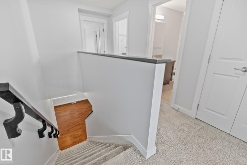 Upper-level landing featuring light-toned carpet, a white banister with a dark wood-finish cap, and solid white doors with brushed nickel hardware - 614 Mcdonough Link, Edmonton, AB 