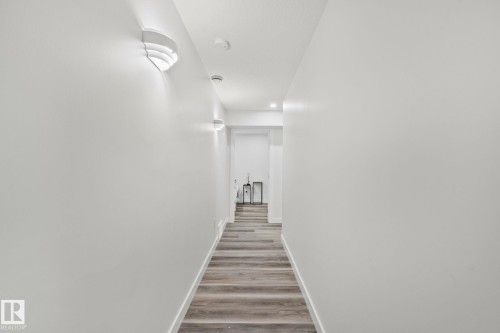 Hallway featuring wood-finish flooring, white baseboards, sconce lighting, and recessed ceiling lights - 614 Mcdonough Link, Edmonton, AB 