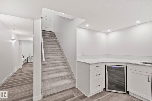 Lower-level wet bar featuring white cabinetry, light-toned countertops, an undermount sink, and an integrated beverage refrigerator - 614 Mcdonough Link, Edmonton, AB 