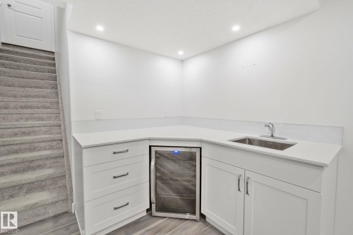 Corner wet bar featuring white cabinetry, light-toned countertops, an undermount stainless steel sink, and an integrated beverage refrigerator - 614 Mcdonough Link, Edmonton, AB 
