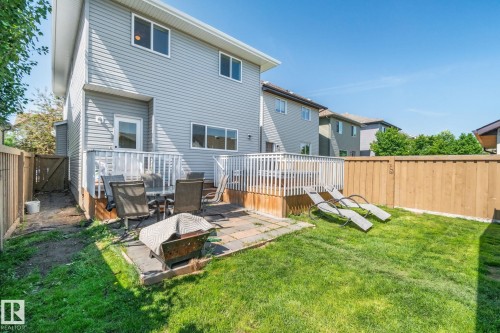 Rear exterior featuring light grey siding, a wood deck with white railings, a ground-level patio, and a fenced yard with grass - 614 Mcdonough Link, Edmonton, AB 