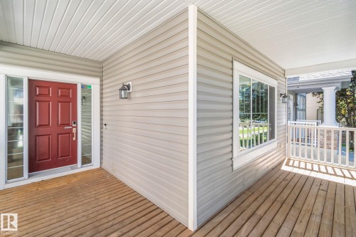 Front porch featuring a red entry door with sidelights, neutral-toned siding, and wood-finish decking - 614 Mcdonough Link, Edmonton, AB 