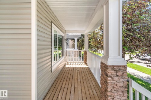 Expansive front porch featuring wood-finish flooring, a white railing, and stone-clad pillars - 614 Mcdonough Link, Edmonton, AB 