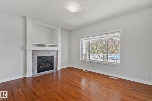 Living space featuring a tiled fireplace with an integrated media niche, rich wood-finish flooring, and a large window with white trim - 614 Mcdonough Link, Edmonton, AB 