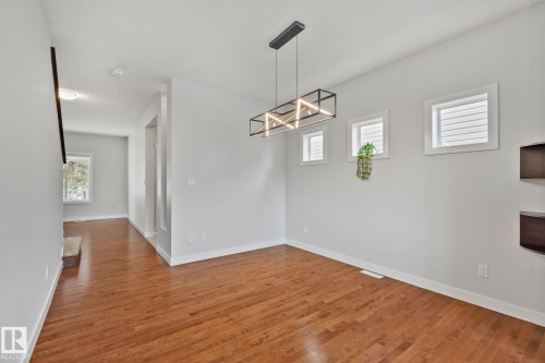 Dining area featuring wood-finish flooring, a modern linear chandelier, and three square windows - 614 Mcdonough Link, Edmonton, AB 