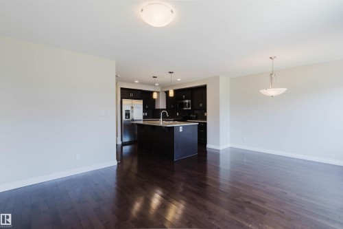 Open-concept living area featuring dark wood-finish flooring, a contemporary ceiling light fixture, and a kitchen with dark cabinetry, stainless steel appliances, and a central island - 1131 177 Street, Edmonton, AB 