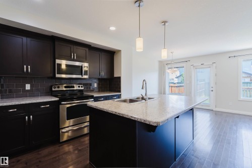 Kitchen featuring dark wood cabinetry, stainless steel appliances, a tile backsplash, and a central island with a double basin sink and a light-colored countertop - 1131 177 Street, Edmonton, AB 