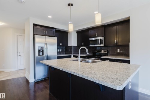 Modern kitchen featuring a central island with a double stainless steel sink and light granite-finish countertop - 1131 177 Street, Edmonton, AB 