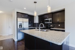 Modern kitchen featuring a central island with a double stainless steel sink and light granite-finish countertop - 
