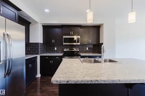 Kitchen featuring wood-finish flooring, dark cabinetry with stainless steel hardware, and a subway tile backsplash - 1131 177 Street, Edmonton, AB 