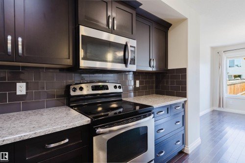 Kitchen featuring dark wood cabinetry, stainless steel oven and microwave, light speckled countertops, and a dark subway tile backsplash - 1131 177 Street, Edmonton, AB 
