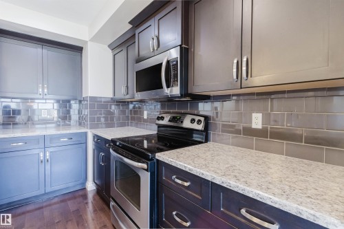 Contemporary kitchen featuring dark wood cabinetry, light speckled countertops, a stainless steel electric range, and an over-range microwave - 1131 177 Street, Edmonton, AB 
