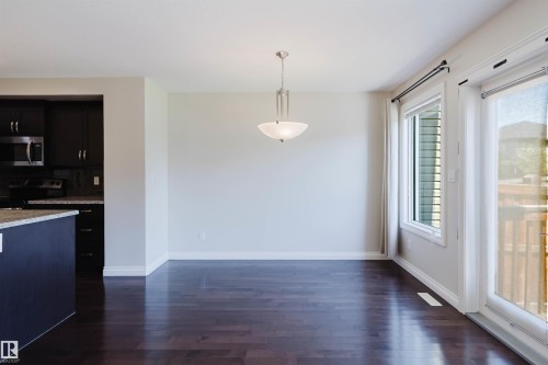 Open concept living space featuring dark wood-finish flooring, a contemporary chandelier, and a sliding glass door providing exterior access - 1131 177 Street, Edmonton, AB 