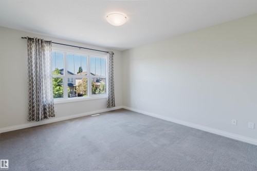 Bright interior space featuring a large window with white trim, light gray wall paint, and complementing gray carpeting - 1131 177 Street, Edmonton, AB 