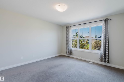 Bright interior room featuring a large window with white trim, gray carpet, and white baseboards - 1131 177 Street, Edmonton, AB 