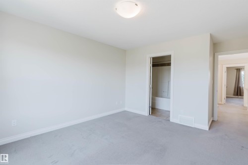 Carpeted interior room with white trim, a semi-flush ceiling light fixture, and an open doorway revealing a tiled bathroom with a tub - 1131 177 Street, Edmonton, AB 