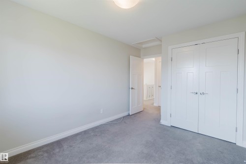 Bedroom featuring a neutral wall color, gray carpeting, a flush mount ceiling light fixture, and white panel doors with brushed nickel hardware - 1131 177 Street, Edmonton, AB 