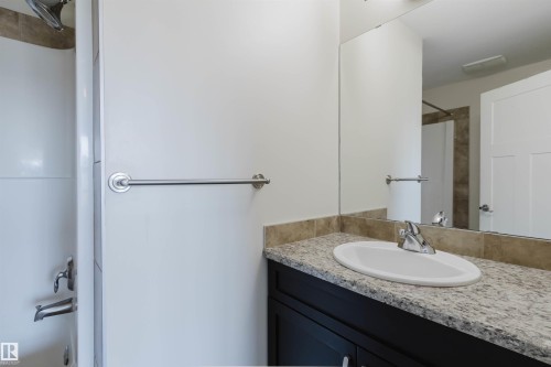 Bathroom vanity featuring a light-toned stone countertop, integrated oval sink, and chrome faucet - 1131 177 Street, Edmonton, AB 