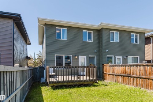 Rear exterior featuring a two-story design with horizontal siding, a ground-level wood deck, multiple windows, and a private fenced yard with natural grass - 1131 177 Street, Edmonton, AB 