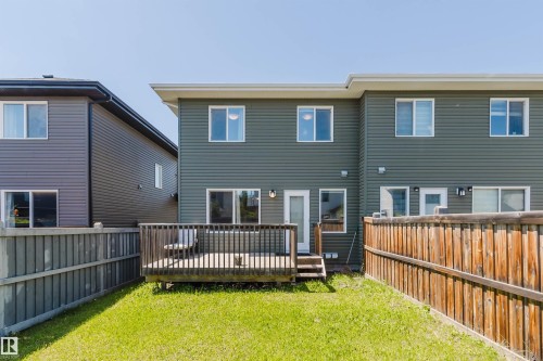 Rear exterior featuring a wooden deck with railing, a grass lawn, and a light wood privacy fence - 1131 177 Street, Edmonton, AB 