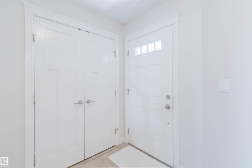 Entryway featuring a white paneled door with transom windows, a double-door closet with satin nickel hardware, and light-toned flooring - 1131 177 Street, Edmonton, AB 