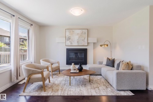 Living area featuring dark wood-finish flooring, a fireplace with a black insert, white baseboards, and multiple windows providing natural light - 1131 177 Street, Edmonton, AB 