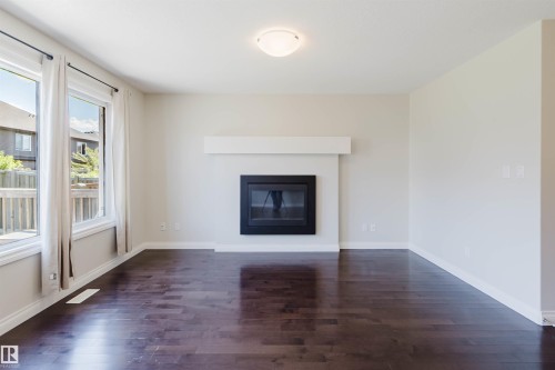 Living area featuring a modern fireplace with a white mantel, dark wood-finish flooring, and multiple windows with white trim - 1131 177 Street, Edmonton, AB 