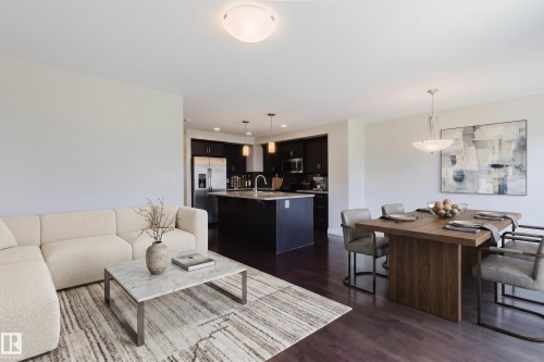 Open-concept living space featuring wood-finish flooring, a kitchen with dark cabinetry, and a central island with countertop seating - 1131 177 Street, Edmonton, AB 