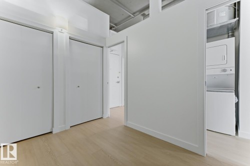 Entryway featuring two white bifold closet doors, light wood-finish flooring, and a concealed stacked washer and dryer unit - 404 10024 Jasper Avenue, Edmonton, AB 