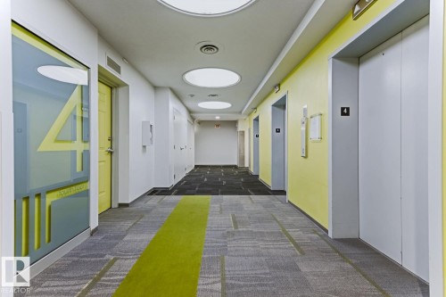 Hallway featuring patterned carpet flooring with a central green stripe, circular recessed lighting, and pale yellow wall accents - 404 10024 Jasper Avenue, Edmonton, AB 