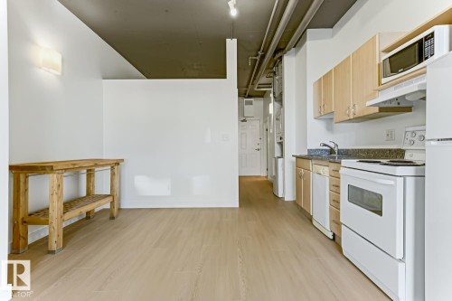 Kitchen area featuring light wood-finish flooring, light wood cabinetry, white appliances, and a dark speckled countertop - 404 10024 Jasper Avenue, Edmonton, AB 