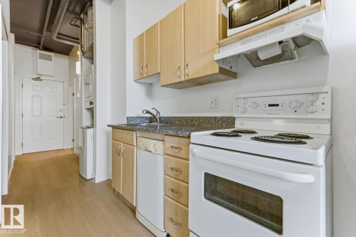 Compact kitchen featuring light wood cabinetry, stone-finish countertops, and a white electric range with an overhead microwave - 404 10024 Jasper Avenue, Edmonton, AB 