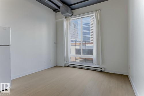Bright interior featuring wood-finish flooring, a large window, white walls, and exposed ductwork - 404 10024 Jasper Avenue, Edmonton, AB 
