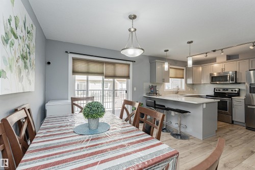 Open-concept dining area and kitchen featuring wood-finish flooring, light grey cabinetry, stainless steel appliances, and a central island with bar seating - 35 675 Albany Way, Edmonton, AB 