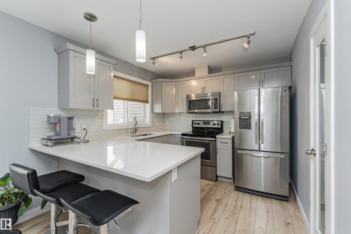 Contemporary kitchen featuring light gray cabinetry, stainless steel appliances, white countertops, and wood-finish flooring - 35 675 Albany Way, Edmonton, AB 