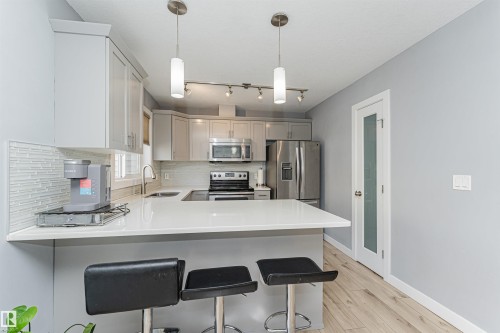 Contemporary kitchen featuring light gray cabinetry, stainless steel appliances, white countertops, and a white tile backsplash - 35 675 Albany Way, Edmonton, AB 