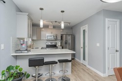 Contemporary kitchen featuring light gray cabinetry, stainless steel appliances, a tile backsplash, light wood-finish flooring, and a breakfast bar with pendant lighting - 