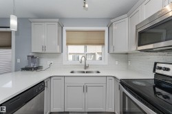 Kitchen featuring light gray cabinetry, white countertops, stainless steel appliances, a tile backsplash, and a double-basin sink - 