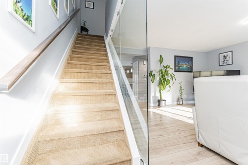Carpeted staircase featuring a light wood-tone handrail and modern glass panel railing - 35 675 Albany Way, Edmonton, AB 