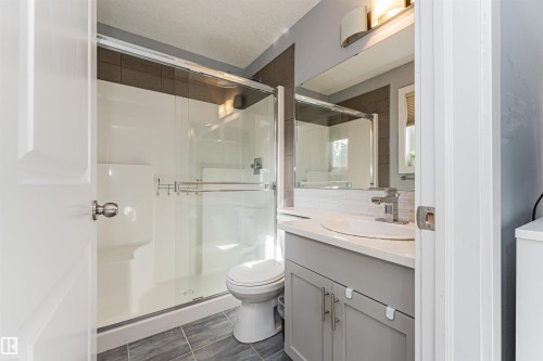 Modern bathroom featuring a glass-enclosed shower, white vanity with an undermount sink, chrome faucet, and contemporary light fixture - 35 675 Albany Way, Edmonton, AB 