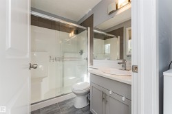 Modern bathroom featuring a glass-enclosed shower, white vanity with an undermount sink, chrome faucet, and contemporary light fixture - 