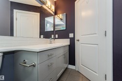 Bathroom vanity featuring a light gray cabinet with brushed nickel hardware, white countertop, and white subway tile backsplash - 