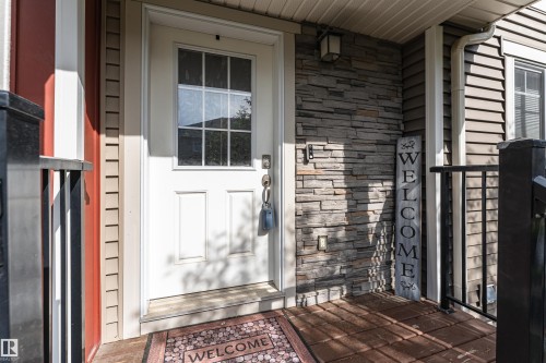 Entryway featuring a white door with divided lites, stacked stone accent siding, dark wood-finish decking, and black metal railings - 35 675 Albany Way, Edmonton, AB 