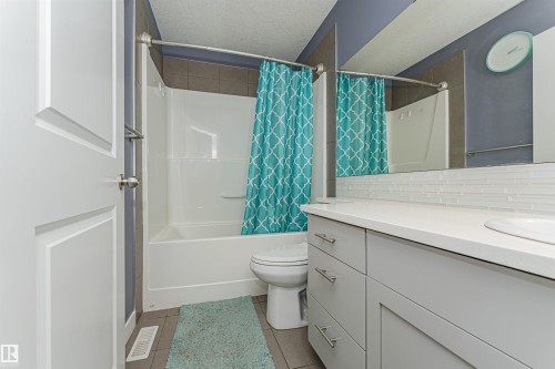 Bathroom featuring a white vanity with dual sinks, a solid surface countertop, and a full-width mirror with a glass tile backsplash - 35 675 Albany Way, Edmonton, AB 