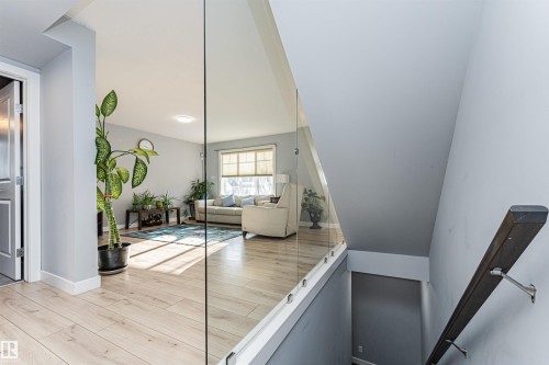 Open-concept living area featuring light wood-finish flooring, a glass panel railing, a window with blinds, and recessed lighting - 35 675 Albany Way, Edmonton, AB 