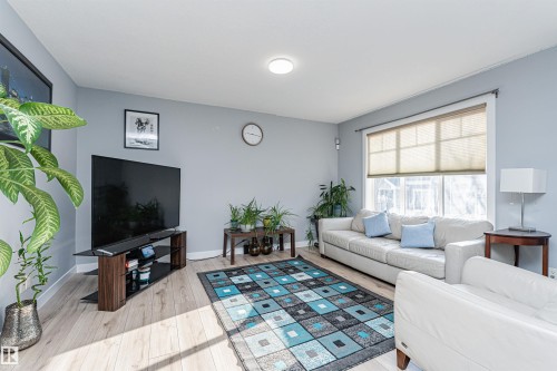 Living room featuring wood-finish flooring, light blue wall paint, a large window with blinds, and recessed lighting - 35 675 Albany Way, Edmonton, AB 